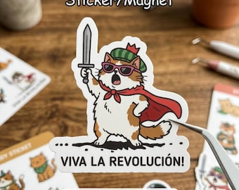 May include: A sticker or magnet featuring a cartoon cat with sunglasses, a red cape, and a sword, with the text "VIVA LA REVOLUCIÓN!" The cat is wearing a green hat with a red crown. Other cat stickers are in the background.