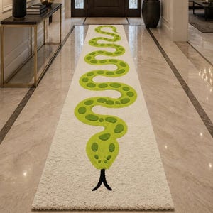 May include: A long, rectangular runner rug featuring a cream-coloured background with a large, winding lime green snake pattern. The snake has darker green circular spots along its body and a black, forked tongue at the head of the design.