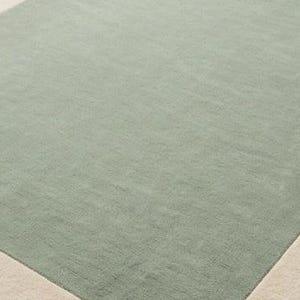 K&ouml;nnte beinhalten: Ein rechteckiger Teppich mit einer gro&szlig;en salbeigr&uuml;nen Mittelfl&auml;che, die von einem einfarbigen cremefarbenen Rand umgeben ist. Der Teppich hat eine kurze, dichte Florstruktur, die auf der gesamten Oberfl&auml;che gleichm&auml;&szlig;ig erscheint und ein schlichtes Design bildet.