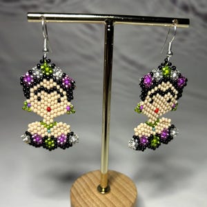 Puede incluir: Una taza de cerámica blanca con un asa negra y el texto "But First, Coffee" en negrita negra. La taza se encuentra sobre un fondo borroso, sugiriendo un ambiente acogedor.