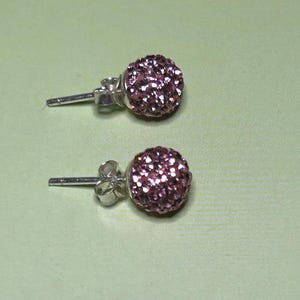 A pair of purple glitter earrings with a silver post and ear hooks, resting on a green surface.