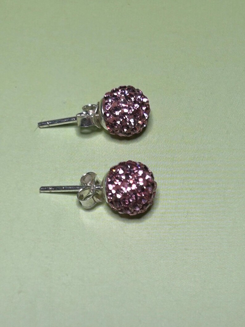 A pair of purple glitter earrings with a silver post and ear hooks, resting on a green surface.