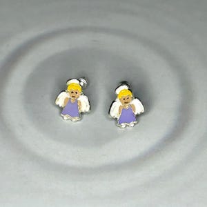 two small silver earrings with angel designs, placed on a gray surface.