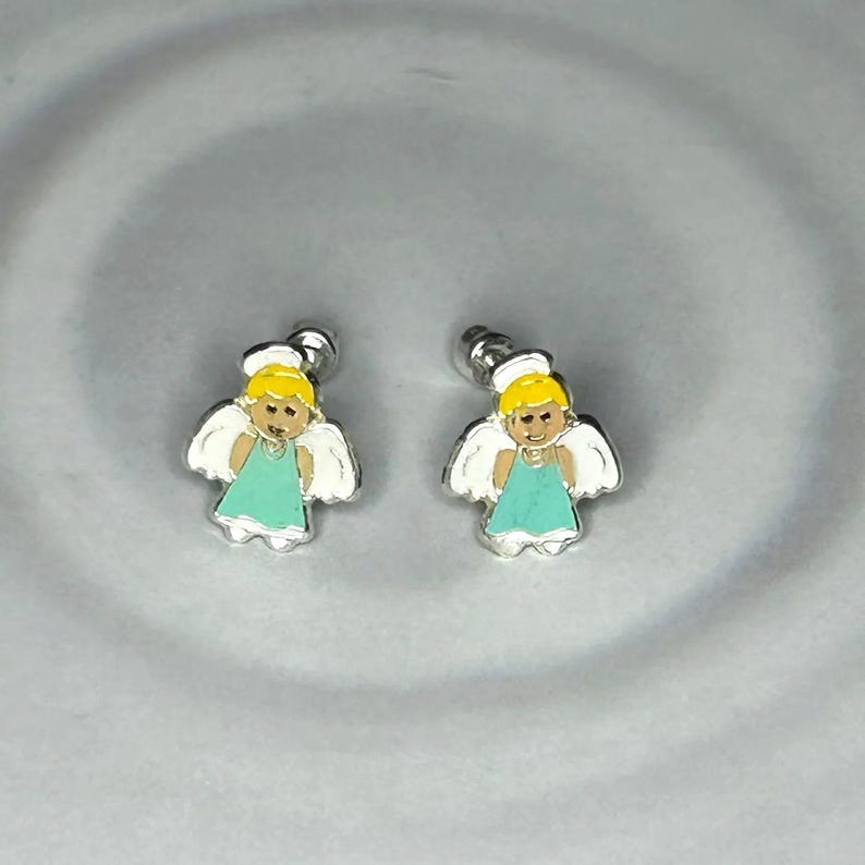 A pair of silver earrings with small, cartoon-like figures of angels on a gray background.