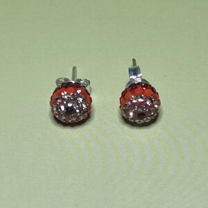 A pair of red and silver earrings with rhinestones or crystals on a light green background.