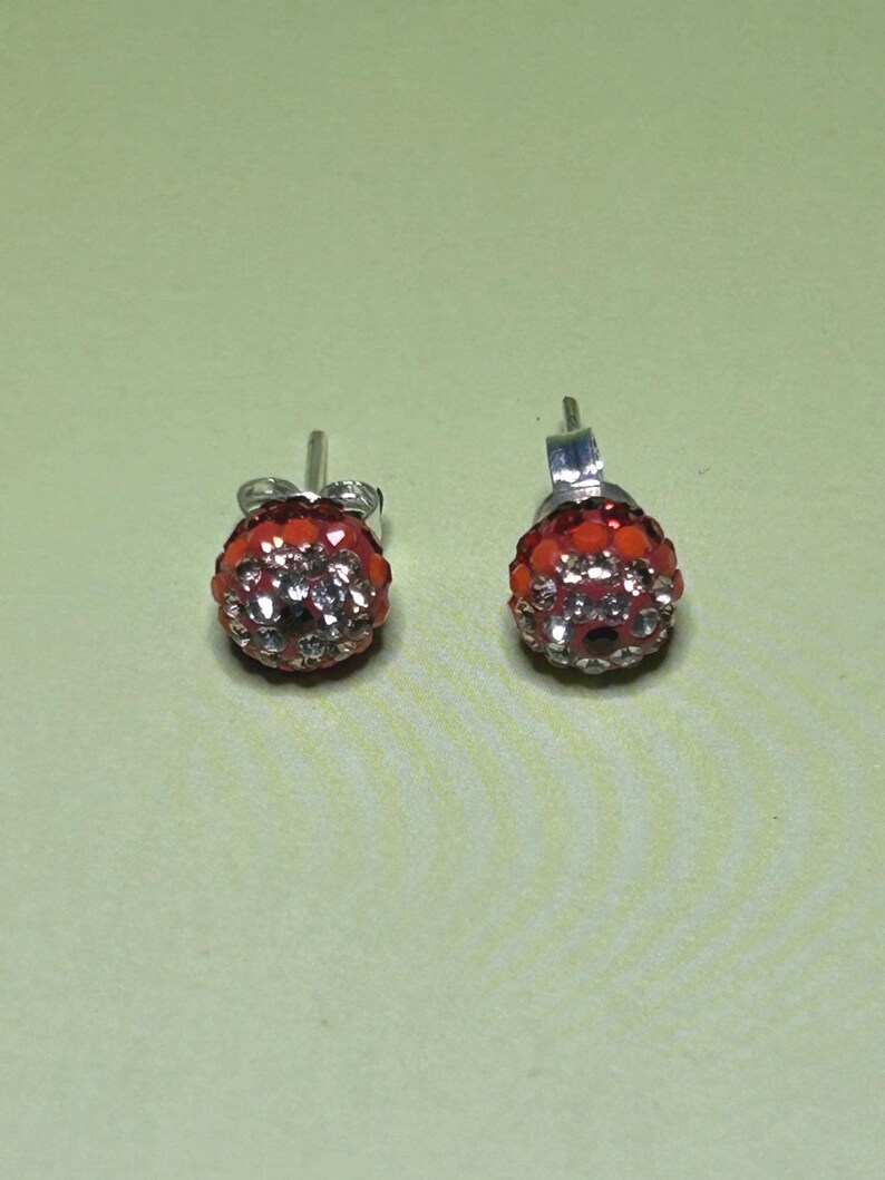 A pair of red and silver earrings with rhinestones or crystals on a light green background.