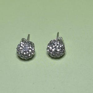 A pair of silver earrings with small, round, sparkling stones on a light green background.
