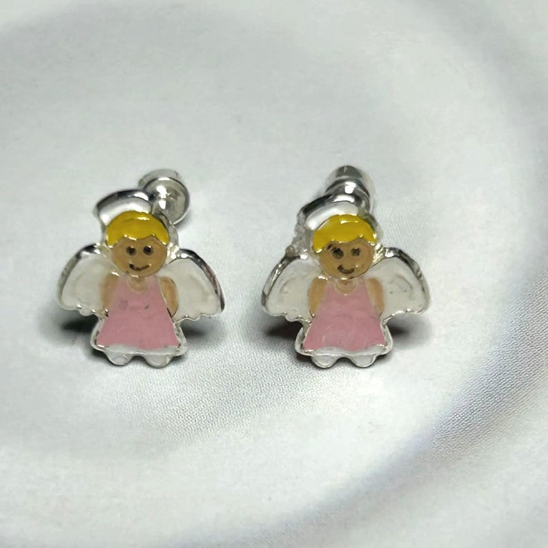 A pair of silver earrings with small, cartoon-like figures of angels wearing pink dresses.