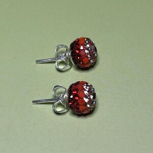 A pair of red and silver earrings with rhinestones or crystals on a green background.