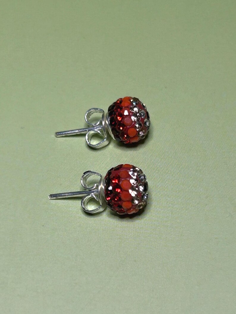 A pair of red and silver earrings with rhinestones or crystals on a green background.