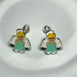 A pair of silver earrings with small, cartoon-like figures of angels wearing green dresses.