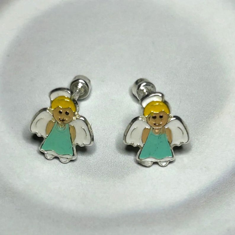 A pair of silver earrings with small, cartoon-like figures of angels wearing green dresses.