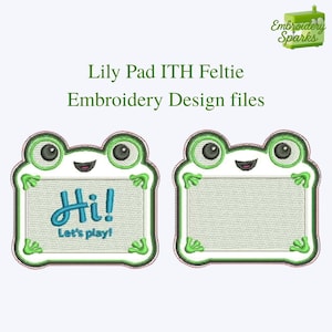 May include: Two embroidered frog-shaped feltie designs. One says "Hi! Let's play!" in blue script. The other is a blank feltie. Both have green and white accents. The text "Lily Pad ITH Feltie Embroidery Design files" is above the designs.
