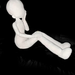 May include: A white, seated doll-like figure with a large head and elongated limbs. The figure is posed with one hand near its head and the other resting on its knee. The doll is set against a black background.