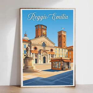 May include: A framed art print featuring a stylized illustration of Reggio Emilia, Italy. The artwork depicts a church, a statue, and a small kiosk under a bright blue sky. The text "Reggio Emilia" is displayed at the top of the print.