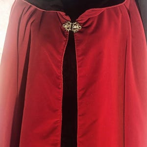 Puede incluir: Una capa de terciopelo rojo con capucha y cierre decorativo. La capa es de color rojo intenso y tiene un forro negro en la capucha. El cierre es dorado y ornamentado. La capa es una prenda clásica, adecuada para disfraces u ocasiones especiales.