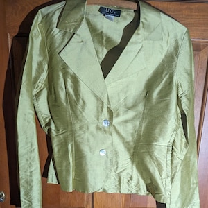 May include: A chartreuse-colored blazer with a notched collar and long sleeves. The blazer has two pearlescent buttons and a tailored fit. The label reads "UC". The garment is hanging on a wooden hanger.