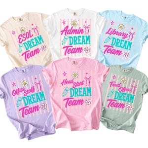 May include: A collection of six short-sleeved crew neck t-shirts in various pastel colors, each featuring a graphic print with vertical stripes, a daisy, a pencil, a bow, and the text 'DREAM TEAM' alongside specific roles like ESOL, Admin, or Library.