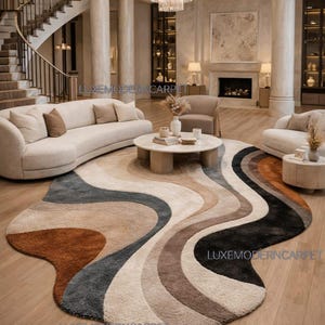May include: A large, abstract rug with a flowing, wave-like design in shades of brown, beige, grey, and black. The rug is in a luxurious living room with a curved sofa, round coffee table, and a chandelier.