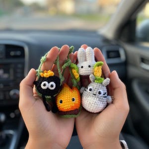 May include: A collection of four small crocheted figures including a black soot sprite with a yellow star, a white rabbit, a flame-shaped character in orange and yellow, and a grey and white creature with small ears and a green leaf on its head.
