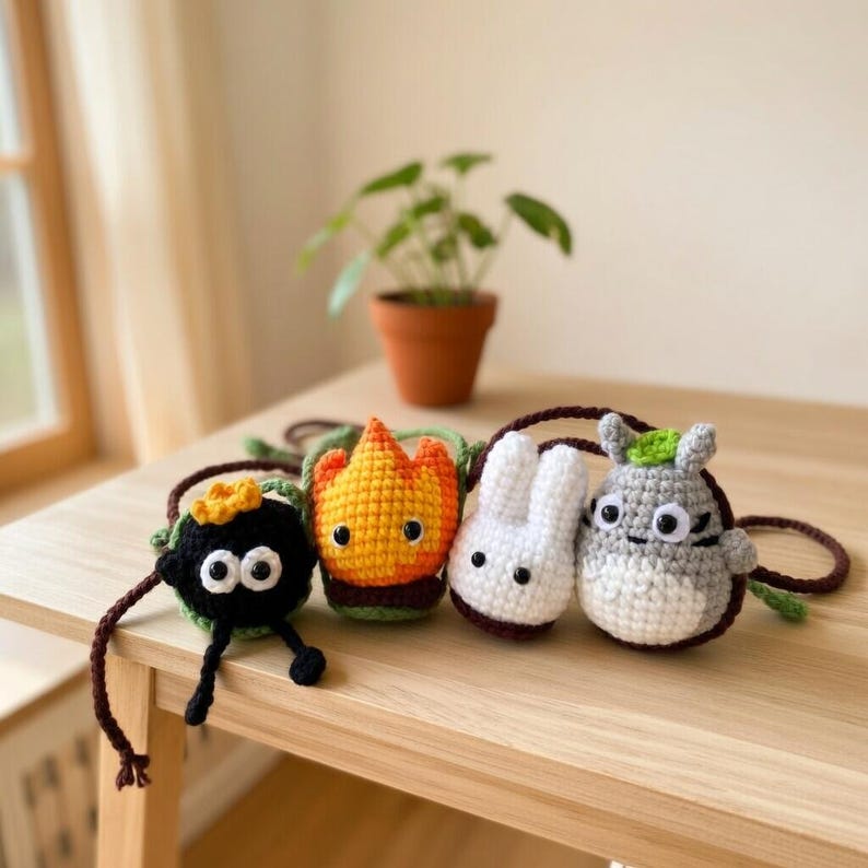 May include: Four small, handmade crochet pouches with long brown straps. The characters include a black soot sprite with a yellow star, a flame-shaped orange and yellow figure, a small white rabbit-like creature, and a grey round creature.