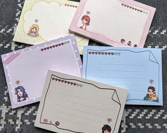 Könnte beinhalten: Ein Set aus fünf bunten Haftnotizblöcken. Jeder Block hat eine andere Pastellfarbe, dekorative Ränder und Illustrationen von Charakteren. Die Blöcke haben herzförmige Akzente und linierte Bereiche zum Schreiben.