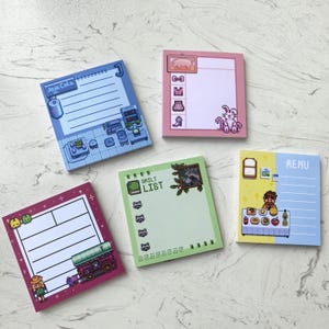 May include: Five square sticky note pads with pixelated art. The pads feature various designs, including a kitchen scene, a pig, a rabbit, a train, a raccoon, and a menu. Each pad has lined space for notes.