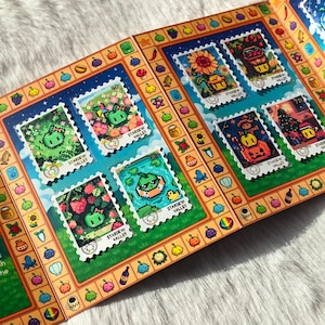 Puede incluir: Folleto abierto con sellos de arte pixelado con el texto "Stardew Valley". Los sellos representan varias escenas, incluyendo un girasol, una casa y una calabaza. El folleto tiene un borde colorido con ilustraciones de frutas y verduras.