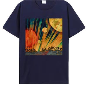 May include: A navy blue t-shirt with a colourful abstract print. The artwork shows celestial bodies and figures in a vibrant watercolour style. The design includes orange and yellow spheres, with figures at the bottom.