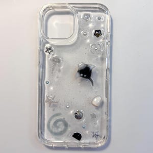 Puede incluir: Funda transparente para teléfono con adornos de temática oceánica. Presenta una manta raya en blanco y negro, estrellas de mar, conchas marinas y perlas. La funda tiene un diseño transparente con un efecto brillante y acuoso.