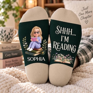 May include: A pair of dark green socks with beige heels and toes. The left sock features a cartoon character reading a book, the name SOPHIA, and floral accents. The right sock displays the text SHHH... I'M READING above an open book graphic.