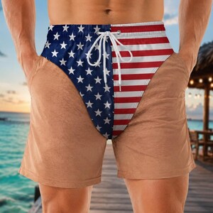May include: Swim shorts featuring a split design with a blue field of white stars on the left and horizontal red and white stripes on the right. The garment includes a white drawstring at the elasticized waistband and two side pockets.