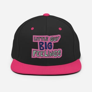 May include: A black baseball cap with a bright pink brim and top button. The front features embroidered text that reads LITTLE GUY BIG FEELINGS in dark blue and light green, set against a textured pink background shape with a dark outline.