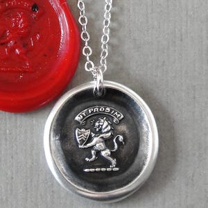 May include: A silver pendant necklace with a round, engraved seal design. The seal features a lion holding a shield, with the words "MY PROSIM" around the edge. A red wax seal with a similar design is next to the pendant.