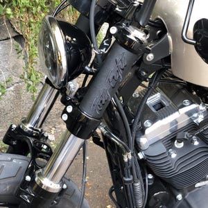 May include: Close-up of a black motorcycle with chrome accents. The handlebars have black grips with the text "Forty Eight". The front forks are silver, and the headlight is black with a chrome bezel. The motorcycle's engine is visible.