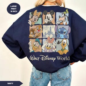 Może przedstawiać: Granatowa bluza z dużym, kolorowym nadrukiem postaci Disneya, w tym Myszki Miki, Myszki Minnie, Goofy'ego i Stitcha. Poniżej nadruku widnieje napis "Walt Disney World". Nadruk na bluzie ma 40.6 cm.