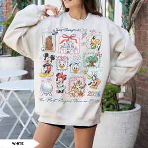 Puede incluir: Sudadera de color crema con un colorido collage de personajes y lugares emblem&aacute;ticos de Disney. El dise&ntilde;o incluye a Mickey Mouse, Minnie Mouse, Donald Duck y Goofy, junto con el texto "Walt Disney World" y "The Most Magical Place on Earth". Tambi&eacute;n se muestra el a&ntilde;o "2026".