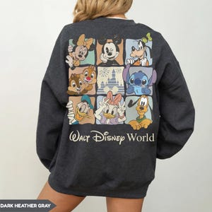 Może przedstawiać: Ciemnoszara bluza z nadrukiem przedstawiającym postacie Disneya, w tym Myszka Miki i Stitch. Poniżej nadruk z napisem "Walt Disney World". Styl casualowy i wygodny.
