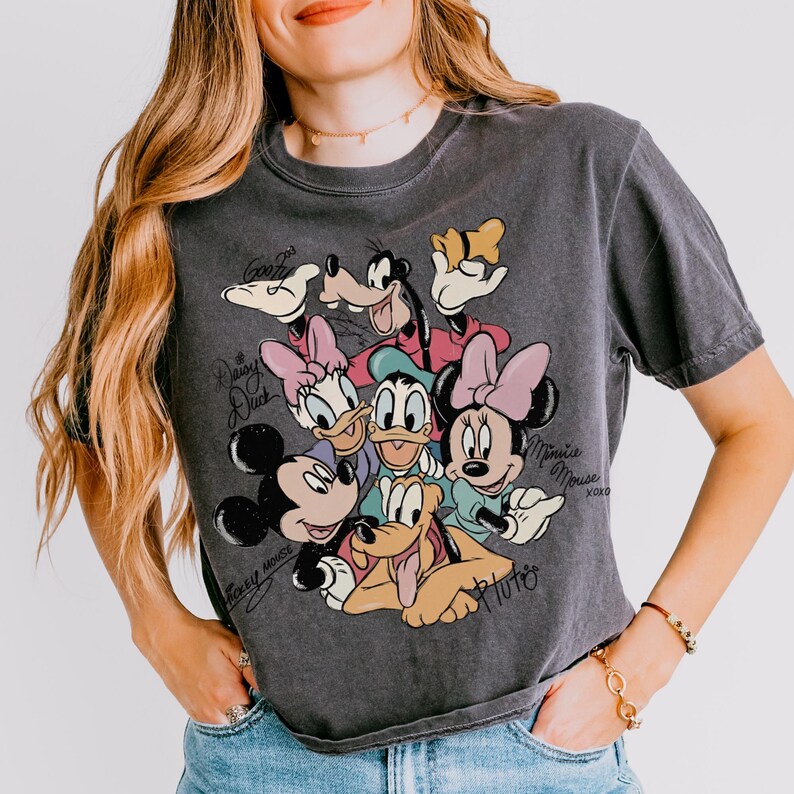 May include: Dark gray t-shirt featuring a colorful graphic of Disney characters including Mickey Mouse, Minnie Mouse, Donald Duck, Daisy Duck, Goofy, and Pluto. The shirt has the characters' names and signatures.