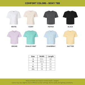 May include: A collection of eight boxy t-shirts in white, ivory, pepper, black, orchid, chalky mint, chambray, and butter. A size chart displays width and length measurements in inches for sizes S through 2XL, ranging from 18.25 to 26 inches wide.