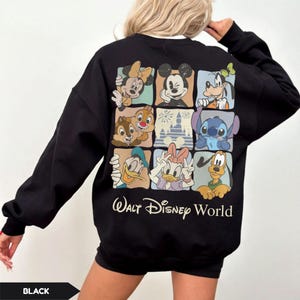 Może przedstawiać: Czarna bluza z nadrukiem przedstawiającym postacie Disneya, takie jak Myszka Miki i Myszka Minnie, Goofy, Kaczor Donald i Kaczka Daisy, Chip i Dale, Stitch i zamek. Pod spodem znajduje się napis "Walt Disney World".