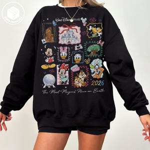 Puede incluir: Sudadera negra con un dise&ntilde;o colorido de Disney World. El dise&ntilde;o incluye varios personajes de Disney y el texto "Walt Disney World", "2026" y "The Most Magical Place on Earth".
