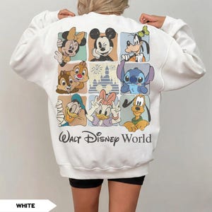 Może przedstawiać: Biała bluza z nadrukiem przedstawiającym postacie Disneya, takie jak Myszka Miki i Myszka Minnie, Goofy, Kaczor Donald i Kaczka Daisy, Chip i Dale, Stitch i Pluto. Pod spodem znajduje się napis "Walt Disney World".