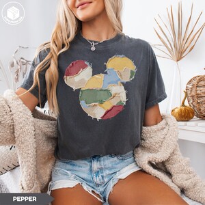 May include: Dark gray t-shirt featuring a patchwork Mickey Mouse design in various colors. The design includes red, yellow, green, and blue patches. The shirt has short sleeves and a crew neck. The word "PEPPER" is printed at the bottom of the image.