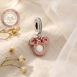 Puede incluir: Un charm en tono oro rosa con una piedra central blanca circular rodeada de circonitas transparentes, rematado con un lazo con piedras rosas. El pasador est&aacute; grabado con PANDORA y S925, con una hilera de piedras transparentes en el borde.