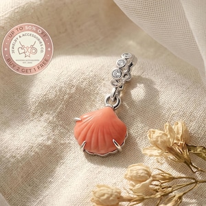 Puede incluir: Un charm de plata con un colgante de concha de color coral. El charm tiene una serie de piedras redondas y transparentes. La imagen incluye el texto "Up to 50% Off" y "Buy 2 Get 1 Free".
