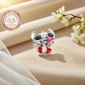 May include: A silver charm shaped like a cartoon character wearing black sunglasses and holding a pink ice cream cone. The character is positioned inside a red and white striped life preserver ring. The charm features detailed metallic textures.
