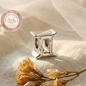 May include: A silver Gemini charm with six clear crystals. The charm is a jewelry accessory. The image includes text that says "Up to 50% Off Jewelry & Accessories Co. Buy 2 Get 1 Free."