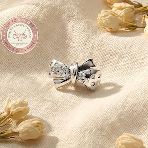Könnte beinhalten: Ein silberner Charme in Schleifenform, verziert mit glitzernden Kristallen. Ein modernes Accessoire für Schmuck. Der Text enthält "Up to 50% Off" und "Buy 2 Get 1 Free".