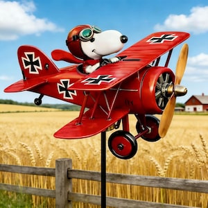 Puede incluir: Decoración de jardín de avión biplano rojo con un personaje de perro de dibujos animados que lleva un casco y gafas de piloto. El avión tiene marcas en blanco y negro y una hélice de madera. El fondo muestra un campo de trigo y un cielo azul.